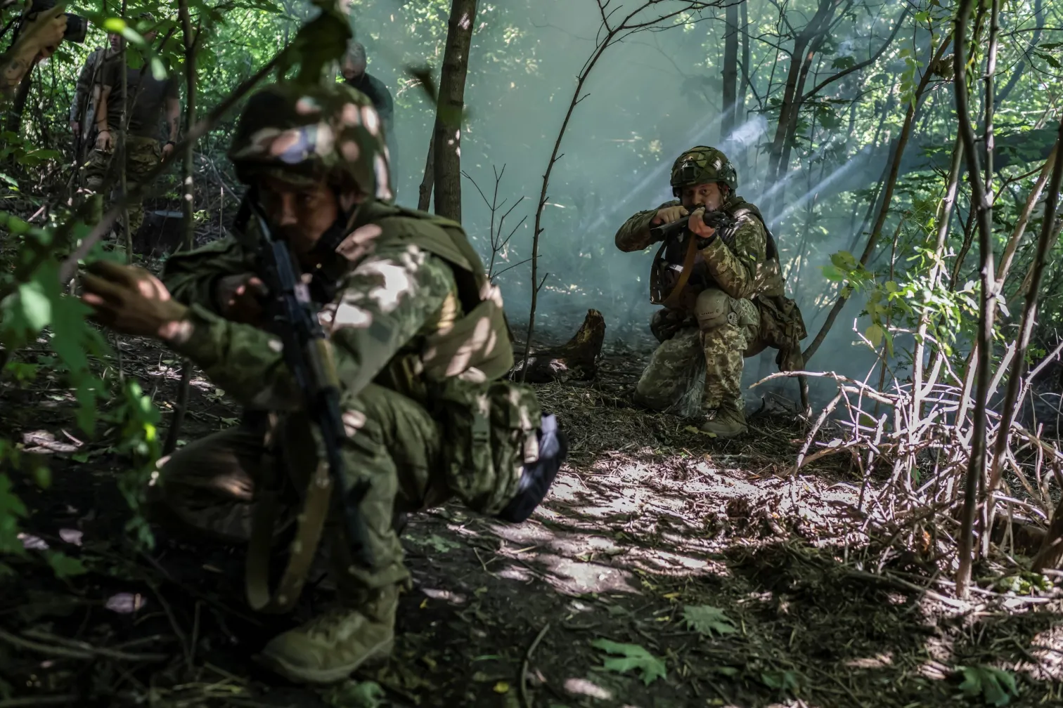 Soldiers moving through wooded terrain under smoke