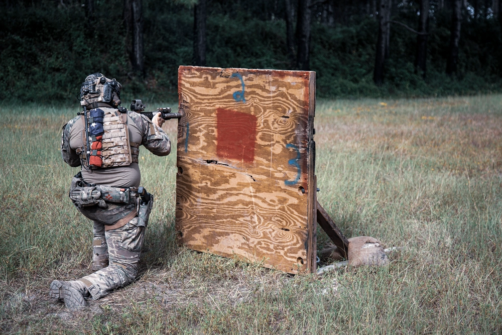 Kneeling operator presenting a weapon around the edge of a wooden barricade